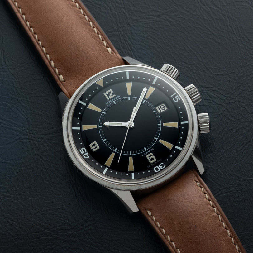 The Jaeger-LeCoultre Tribute to Polaris wristwatch features a brown leather strap and black dial set to 9:15, displayed on a black textured surface.