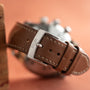 Close-up of a brown leather Jaeger-LeCoultre Tribute to Polaris watch strap, featuring the brands name engraved on the silver buckle, set against a peach background.