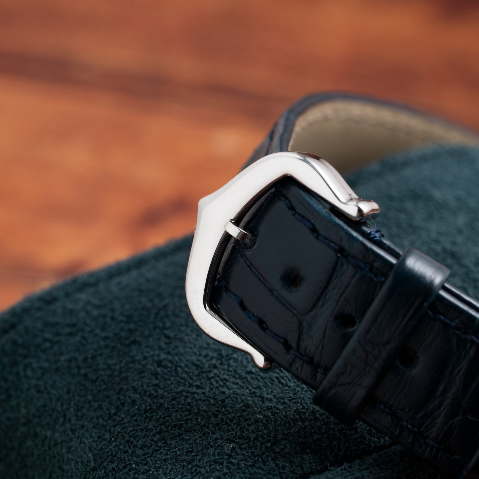 Close-up of a Cartier Tank Cintrée silver buckle on a black leather strap, resting on a textured dark green surface.
