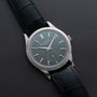 A Patek Philippe Calatrava wristwatch with a silver case and black leather strap displayed on a dark leather surface.