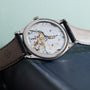 Close-up of the Patek Philippe Calatrava luxury wristwatch with an exposed mechanical movement and leather strap, resting on a book.