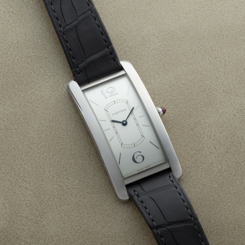 A Cartier Tank Cintrée Limited Edition rectangular wristwatch with a silver face and black leather strap displayed on a beige surface.