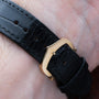 Close-up of the Cartier Tank Louis watch featuring a black leather strap with a gold buckle on a persons wrist.