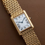 A Cartier Tank Louis watch with a gold case, white rectangular dial, and Roman numerals, displayed on brown leather.