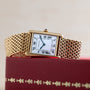 Cartier Tank Louis gold watch featuring a white Roman numeral dial, displayed on a red decorative box.