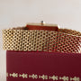 Close-up of the Cartier Tank Louis gold mesh watch band resting on a red textured box with gold decorative accents.