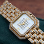 Cartier Ceinture Paris Diamond watch with diamond-encrusted bezel, bracelet, and dial, displayed on a green textured surface.