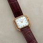 Cartier Ceinture Diamond watch featuring a diamond bezel, white dial, and maroon leather strap displayed on a light surface.