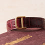 Close-up of the Cartier Ceinture Diamonds burgundy leather strap with a gold D buckle, resting on a textured burgundy surface.