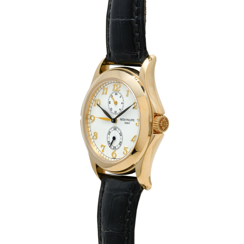 The Patek Philippe Calatrava Travel Time features a gold case, white dial, black leather strap, and two subdials.