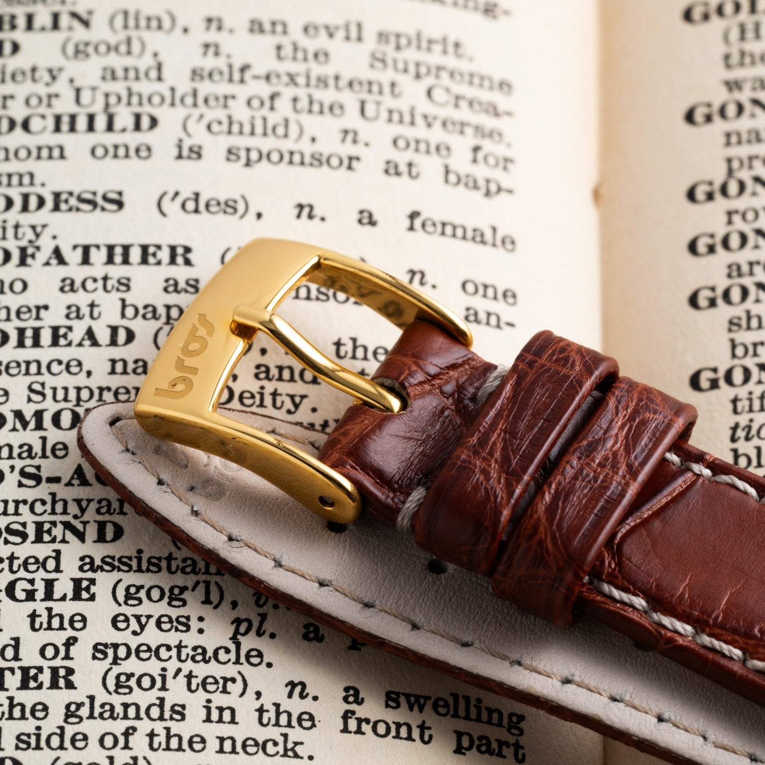 The Piaget Bamboo Dress Watch, featuring a brown leather strap and gold buckle, is displayed resting on an open dictionary page.