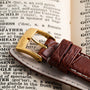 The Piaget Bamboo Dress Watch, featuring a brown leather strap and gold buckle, is displayed resting on an open dictionary page.