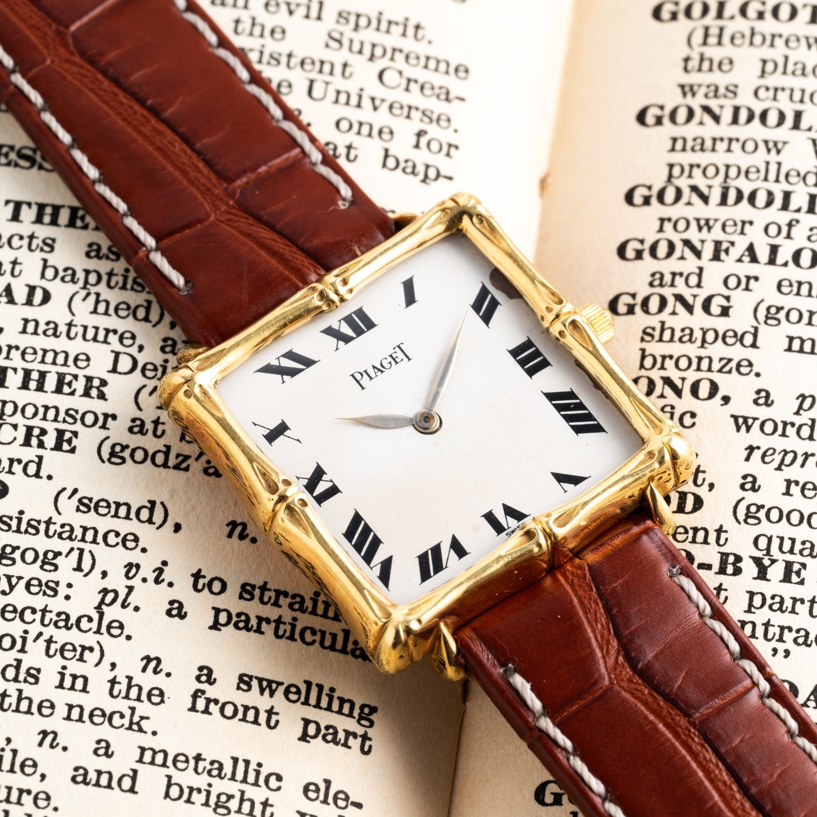 A Piaget Bamboo Dress Watch with a brown leather strap rests on the open pages of an old book.