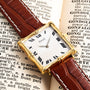 A Piaget Bamboo Dress Watch with a brown leather strap rests on the open pages of an old book.