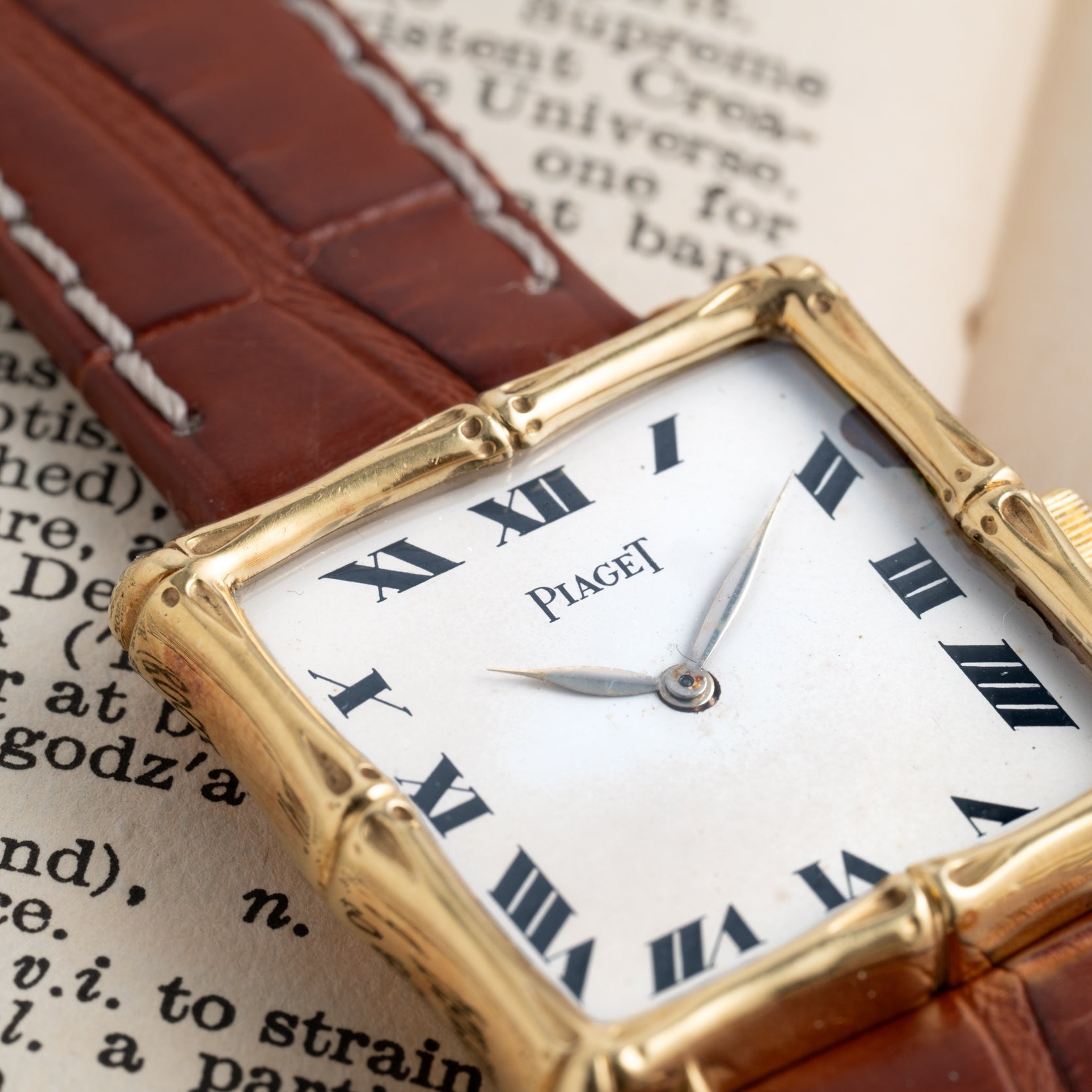 Close-up of a Piaget Bamboo Dress Watch with roman numerals, placed on an open book with text in the background.
