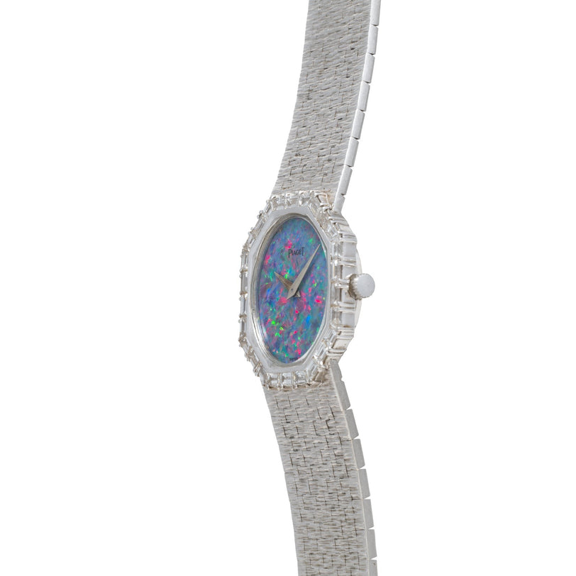 The Piaget Opal White Gold Dress Watch features a textured silver band and a vibrant opalescent face, displayed at an angle.