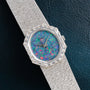 The Piaget Opal White Gold Dress Watch features a colorful opal dial and gem-set bezel, set on a textured band, resting on dark leather.