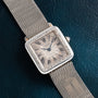 The Cartier Santos Platinum features a square platinum face, diamond bezel, and mesh band, shown against a dark textured background.