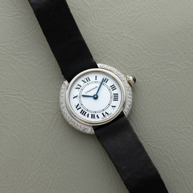 The Cartier Vendome Diamond watch features a black strap, diamond bezel, and Roman numerals on a light gray textured surface.