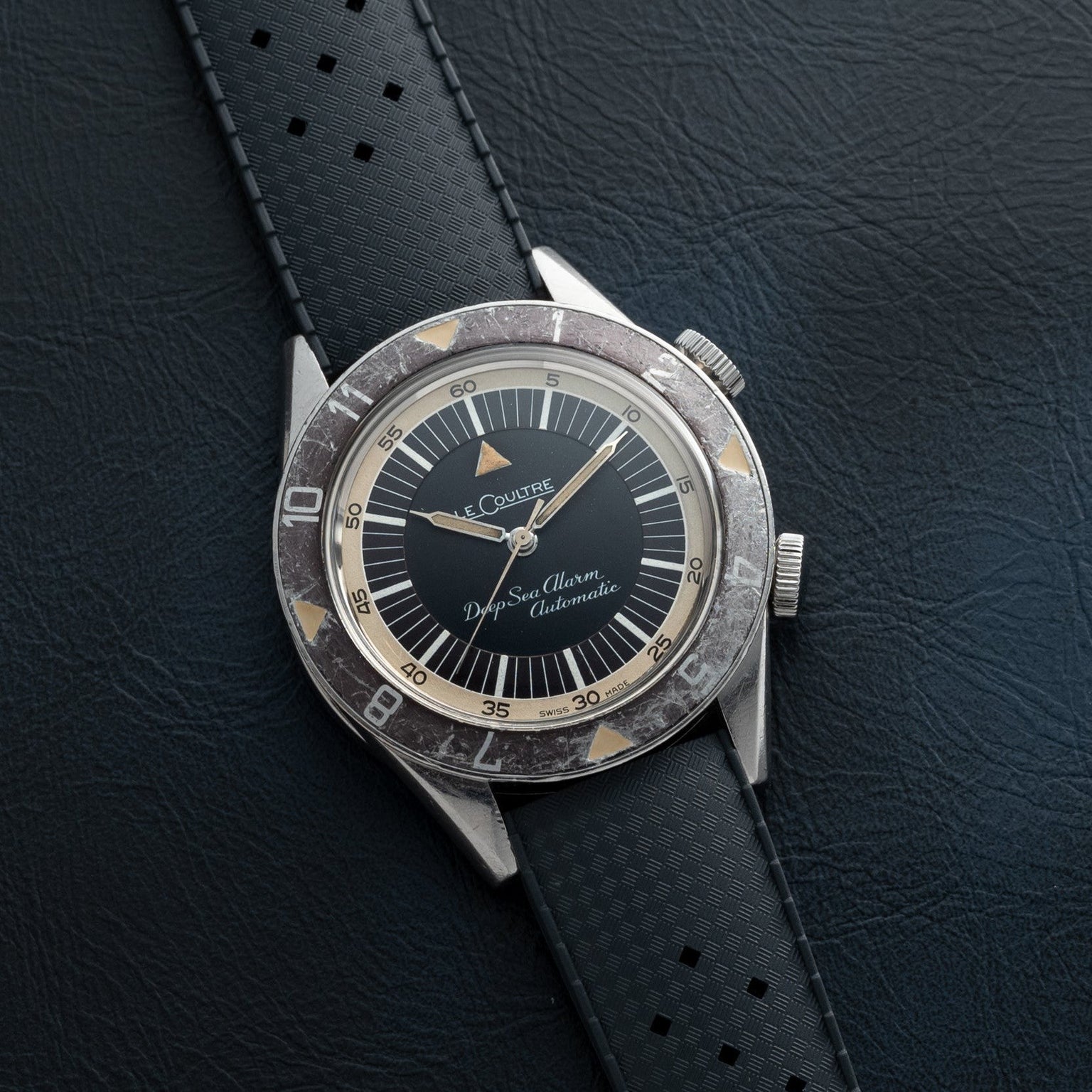 The Jaeger-LeCoultre Deep Sea Alarm U.S. Edition features a black dial and black perforated strap, shown resting on a leather surface.