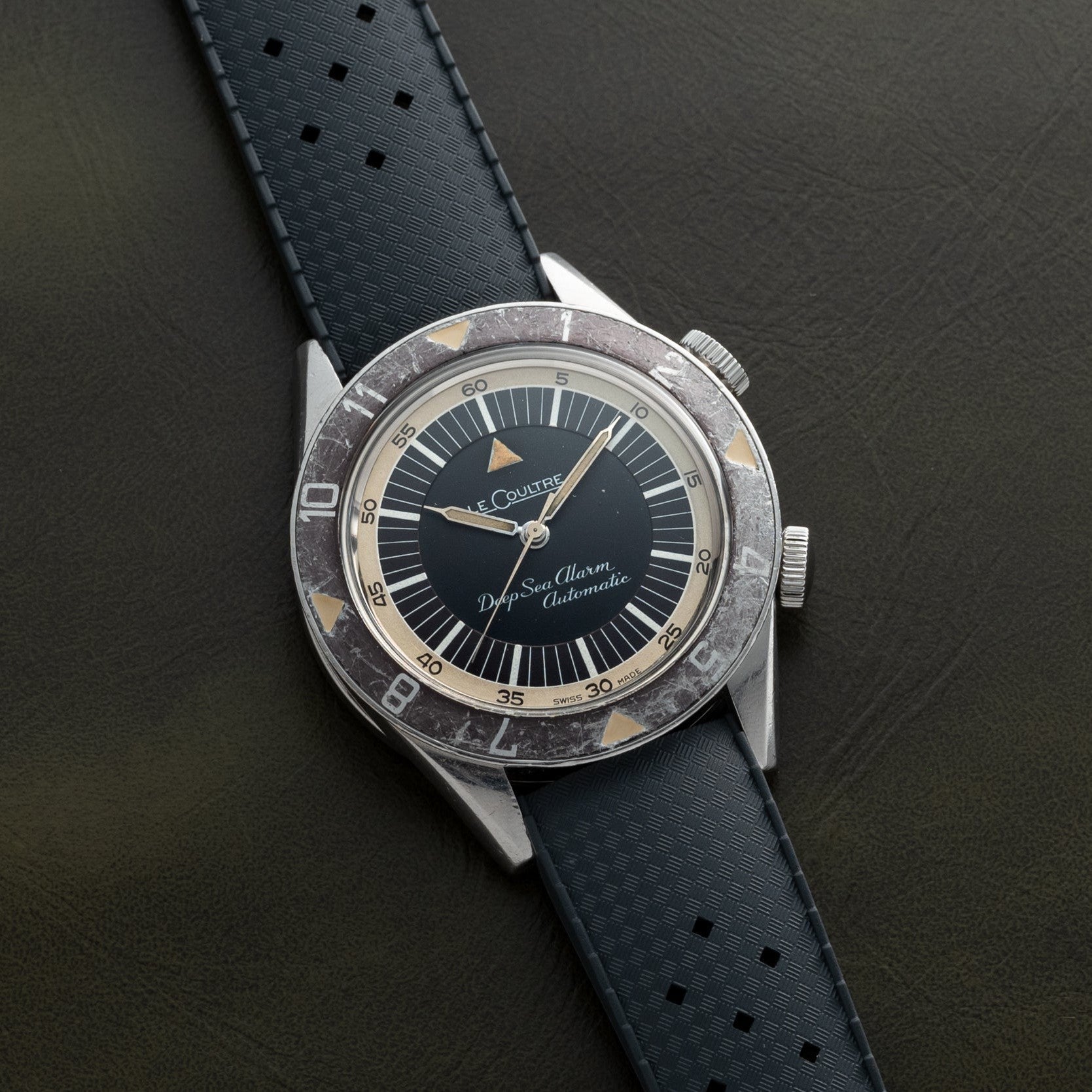 A Jaeger-LeCoultre Deep Sea Alarm U.S. Edition wristwatch with a black strap and black dial displayed on a dark surface.