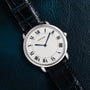 The Cartier Vendome Ronde Louis wristwatch, featuring Roman numerals and a black leather strap, displayed on a dark textured surface.