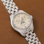 A Patek Philippe Annual Calendar wristwatch in silver with a cream dial and moon phase, displayed on brown leather.