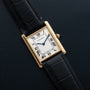 The Cartier Tank Louis Mechaniqúe features a gold case, black leather strap, and Roman numerals on a textured black dial.