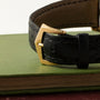 Close-up of the black leather strap with a gold buckle on the Patek Philippe Retrograde Perpetual Calendar watch, resting atop a green hardcover book.