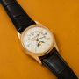 Patek Philippe Retrograde Perpetual Calendar gold watch with moon phase and black leather strap on a mustard yellow surface.