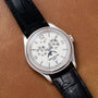The Patek Philippe Annual Calendar Moonphase wristwatch features a black leather strap, elegantly displayed on a brown leather surface.