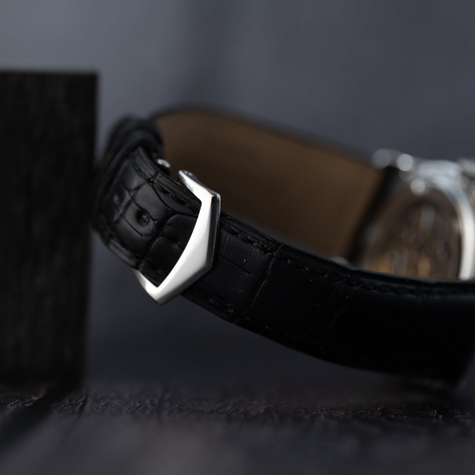 Close-up of the Patek Philippe Annual Calendar Moonphases black leather strap with a silver buckle set against a dark, blurred background.