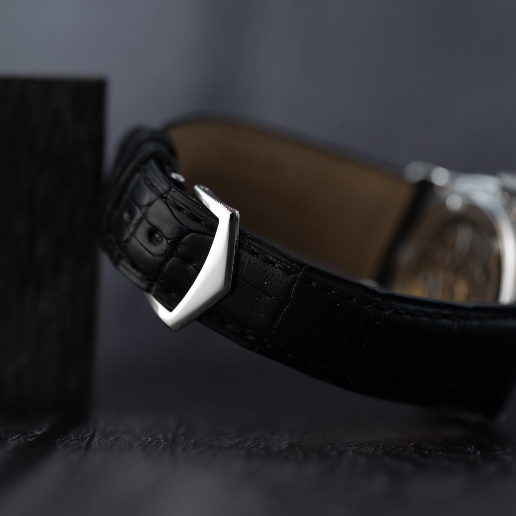 Close-up of the Patek Philippe Annual Calendar Moonphases black leather strap with a silver buckle set against a dark, blurred background.