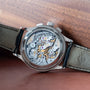 A close-up of the Patek Philippe Chronograph’s intricate exposed mechanical movement and leather strap, displayed on a wooden surface.