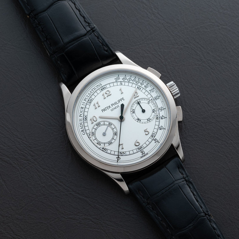 A Patek Philippe Chronograph wristwatch with a white dial and black leather strap displayed on a dark surface.