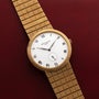 The Patek Philippe Calatrava gold wristwatch features a white Roman numeral dial and a textured band, displayed on a red leather surface.