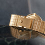 Close-up of the Patek Philippe Calatrava gold watch with a textured metal band, resting on a glossy dark marble surface.