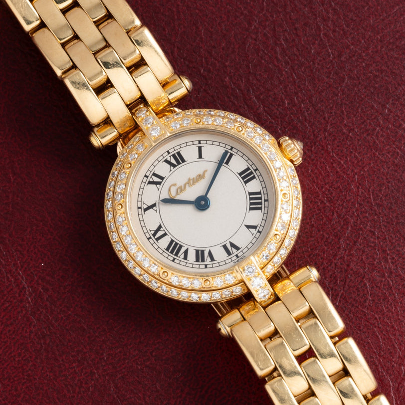 Cartier Panthere Ronde watch with diamond bezel and Roman numerals, shown on a textured burgundy surface.