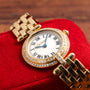 The Cartier Panthere Ronde gold watch with Roman numerals and diamond accents rests on a red textured surface.