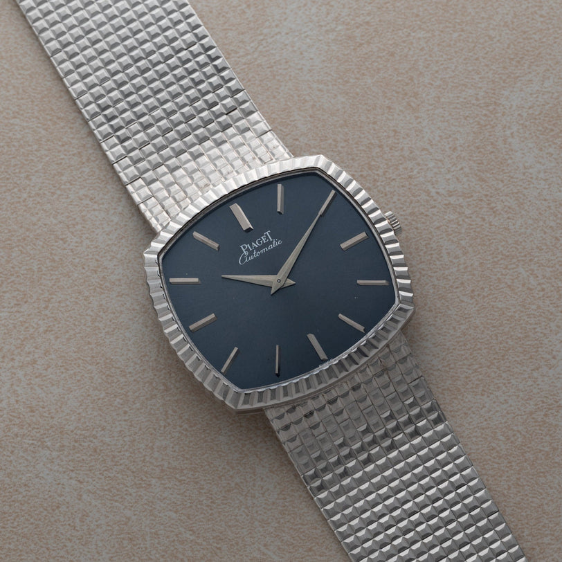 A Piaget Sqound White Gold Dress Watch with a textured band and a blue face is displayed on a light beige surface.