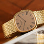 A Patek Philippe Ellipse Jumbo gold watch with a woven band and Roman numerals, resting on a wooden surface.