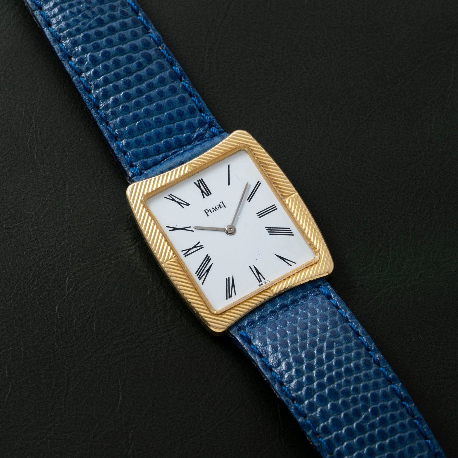 A gold Cartier Protocole watch with a white face, Roman numerals, and a blue textured leather strap on a black background.