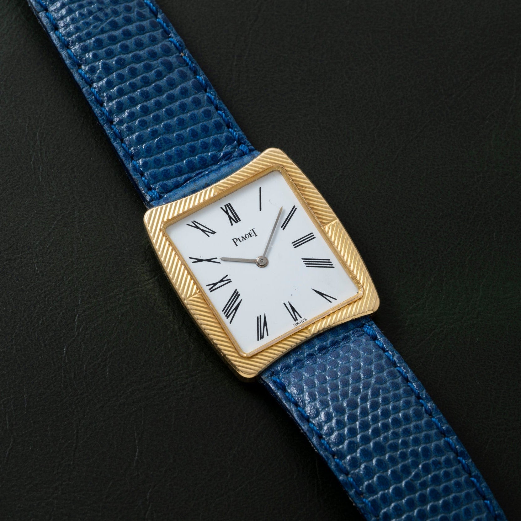 A gold Cartier Protocole watch with a white face, Roman numerals, and a blue textured leather strap on a black background.