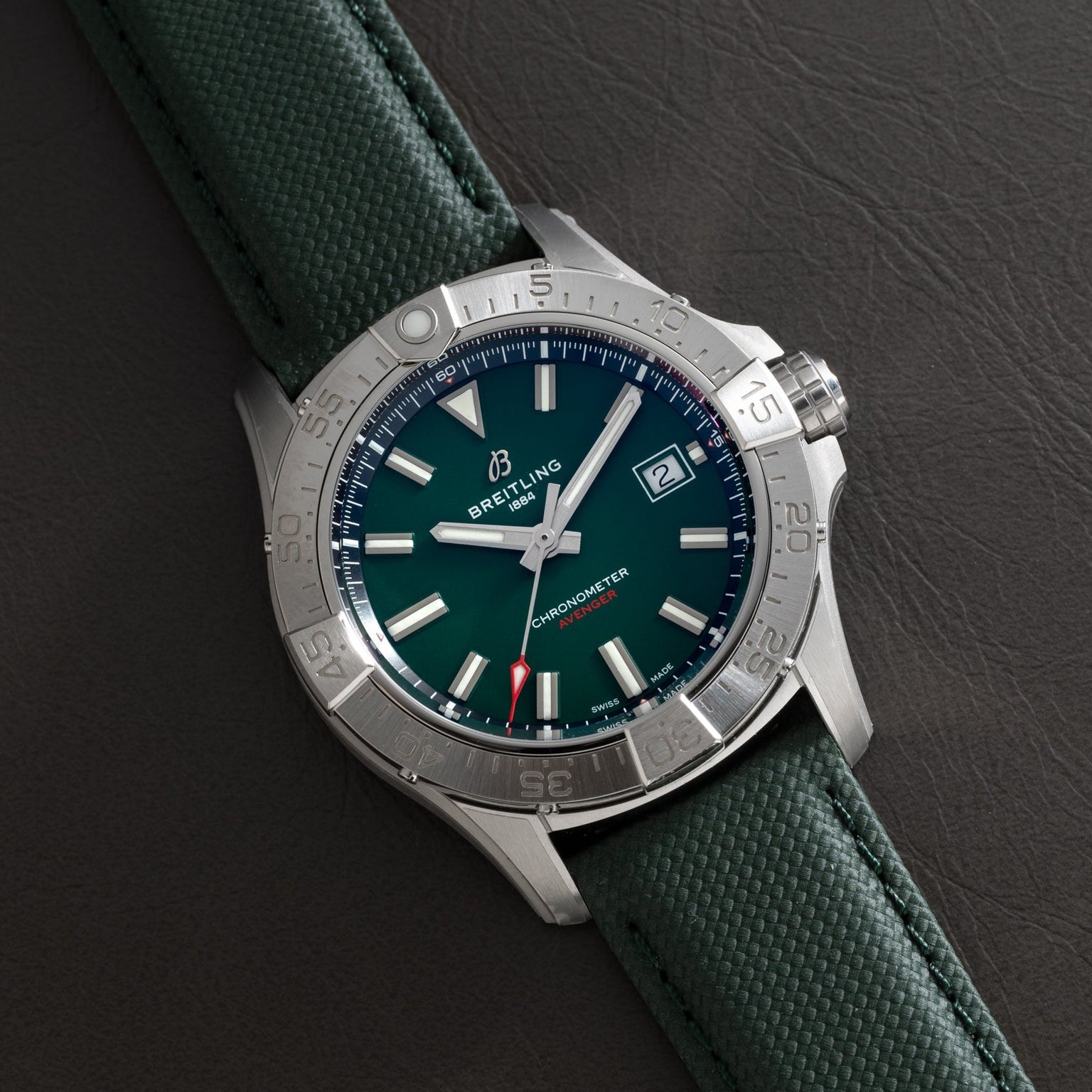 The Breitling Avenger Automatic 42 wristwatch, featuring a green dial and green strap, rests on a dark leather surface.