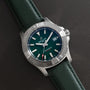 The Breitling Avenger Automatic 42 wristwatch, featuring a green dial and green strap, rests on a dark leather surface.