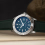 A Breitling Avenger Automatic 42 with a silver case, blue dial, and green strap rests on a light surface.