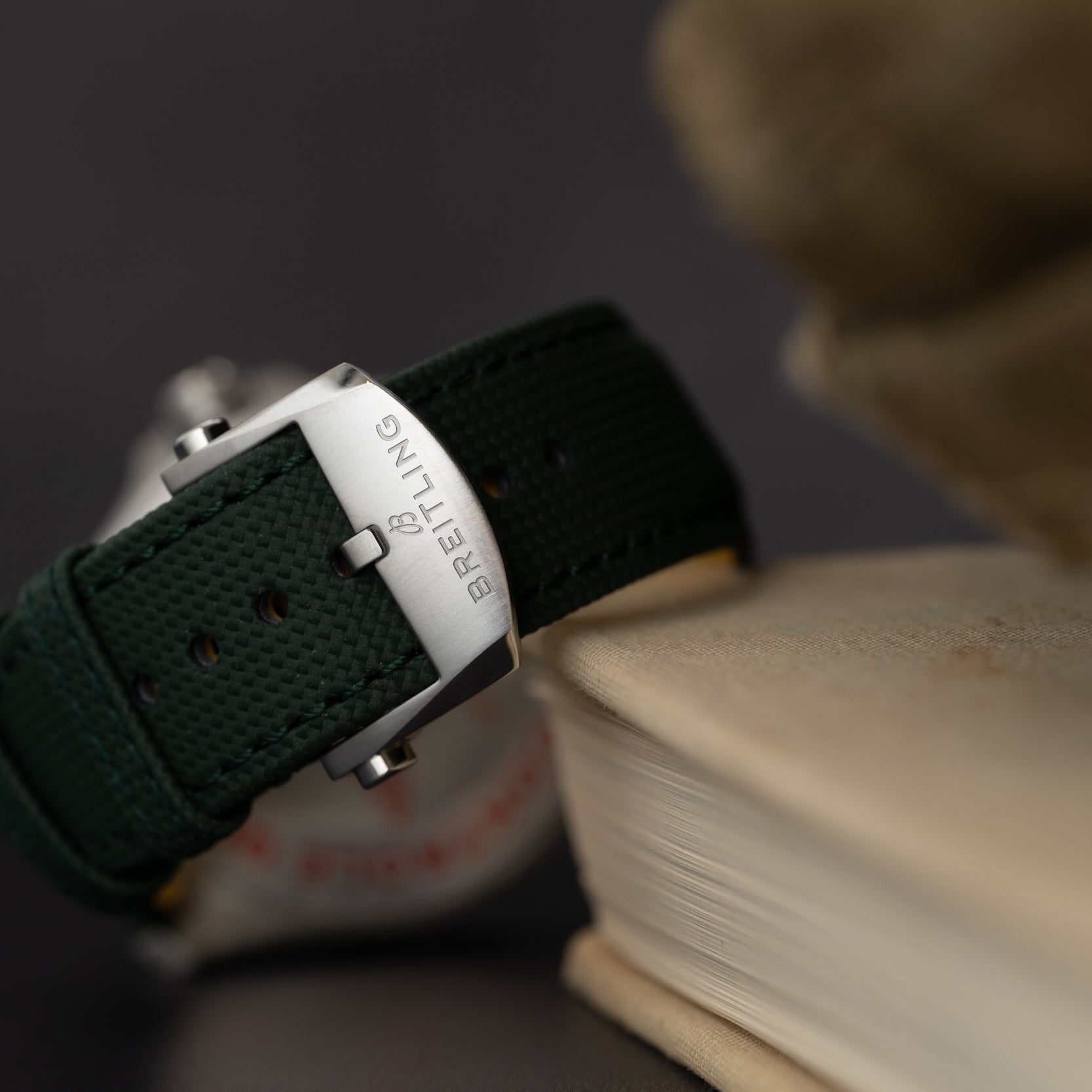 Close-up of a green Breitling Avenger Automatic 42 watch strap and buckle resting on the edge of a closed book.