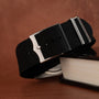 A TUDOR Black Bay Chronograph with a black fabric strap and silver buckle rests on the edge of a closed book.