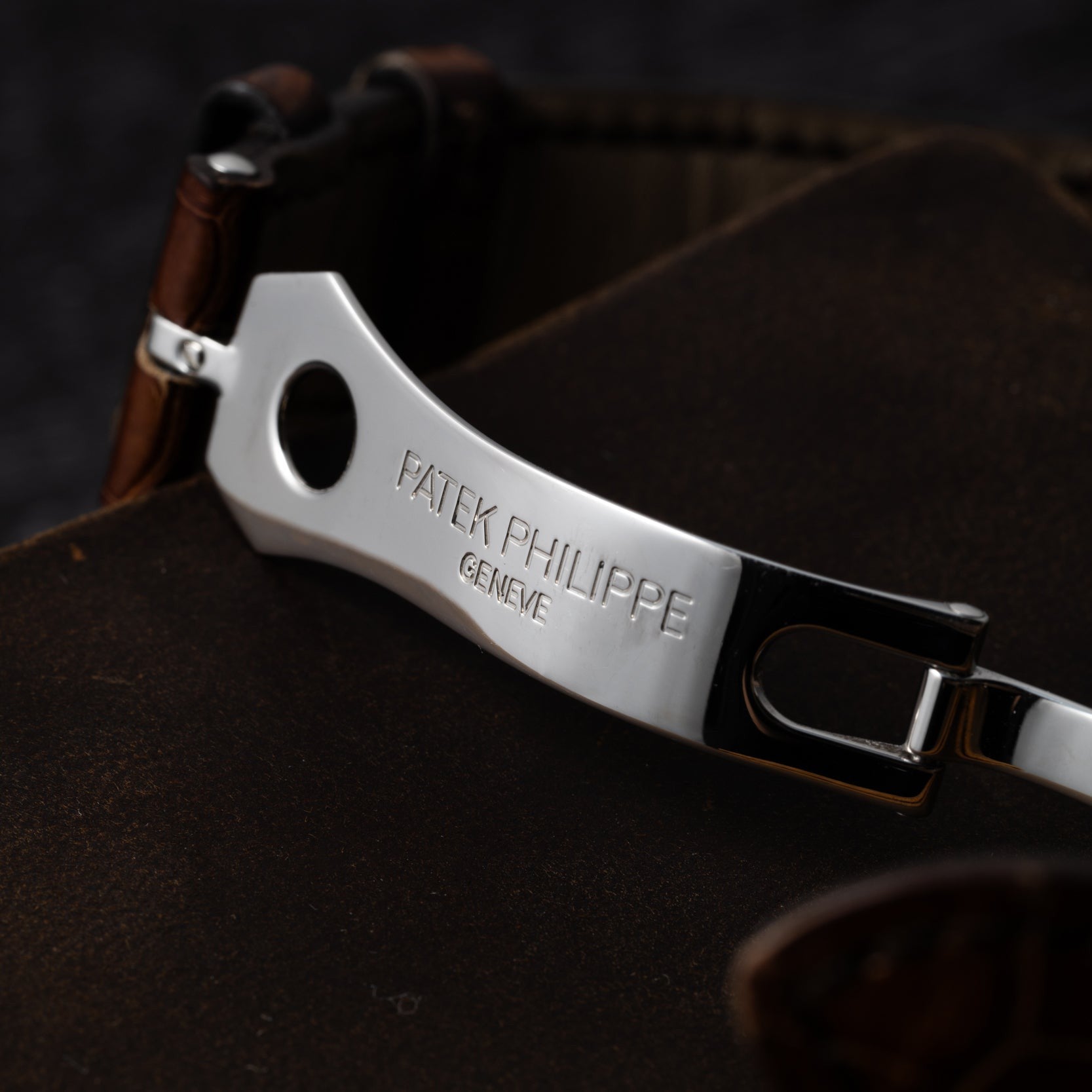 Close-up of a metal Patek Philippe Retrograde Perpetual Calendar watch clasp with a leather strap on a dark surface.