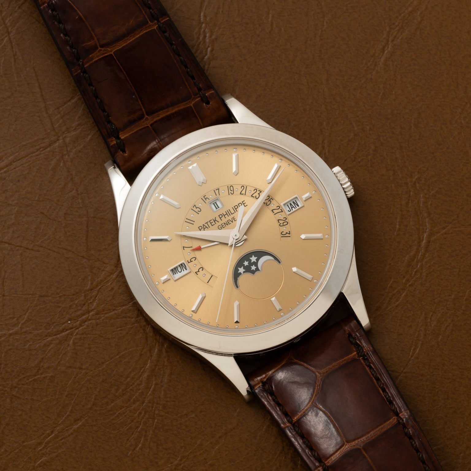 A Patek Philippe Retrograde Perpetual Calendar gold wristwatch with a brown leather strap and moon phase display rests on a brown leather surface.